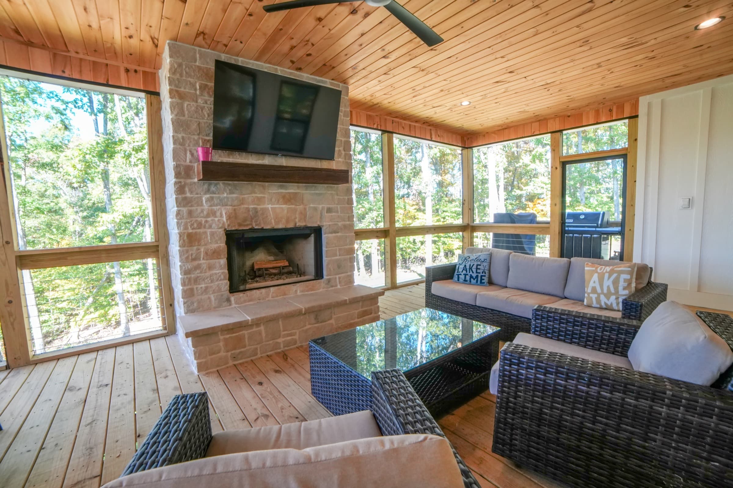 Upper screened porch at Stay at Nolin with stone fireplace lit, lake-time pillows, sectional and dining for six